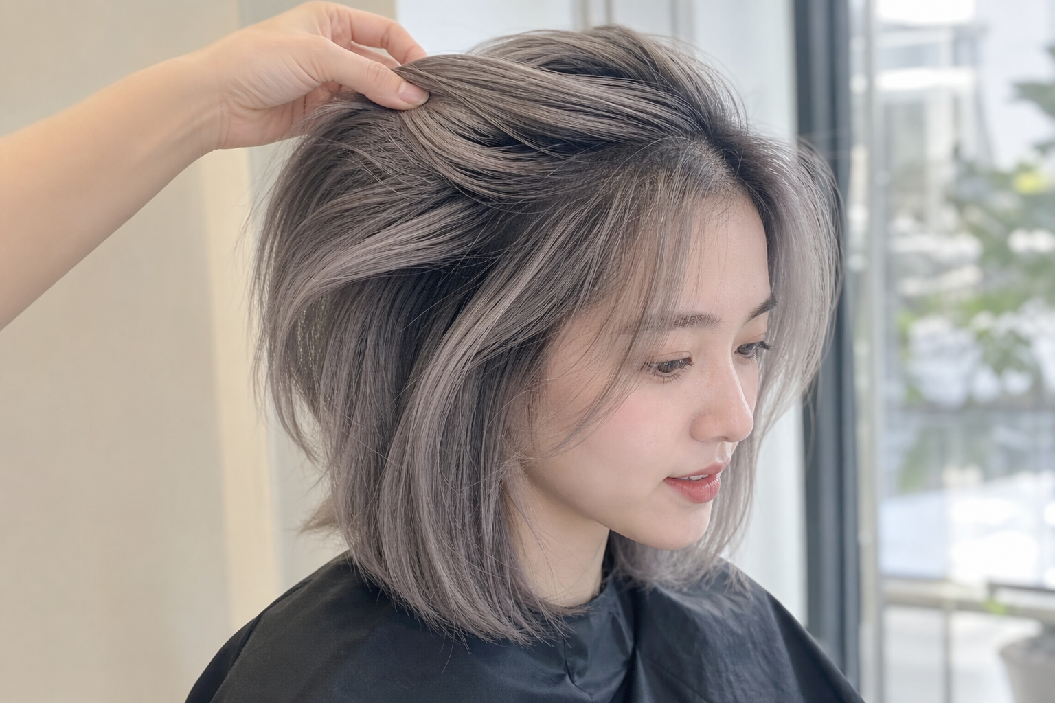 Người phụ nữ với tóc xám khói ngắn đang được chỉnh lại tóc trong không gian sáng gần cửa sổ